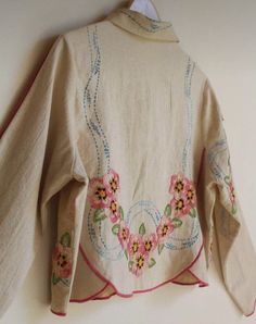 an embroidered jacket hanging on a wall with flowers and leaves in the center, along with pink trimmings