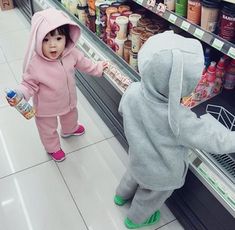 two toddlers are playing in the grocery aisle with each other and one is reaching for food