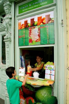 a young boy standing in front of a store selling fruits and vegetables to a woman