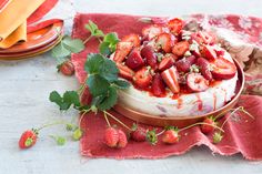 a cake covered in strawberries on top of a red cloth next to plates and utensils