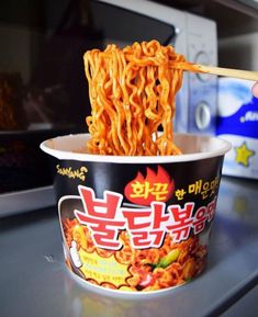 a person holding chopsticks over a bowl of noodles in front of microwave oven