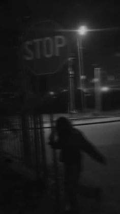 a blurry image of a person walking down the street at night with a stop sign in the background