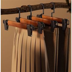 three pieces of pleated skirts hanging on a wooden rail with metal clips attached to them