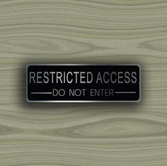 a black and silver sign that says restricted access do not enter on a wood background