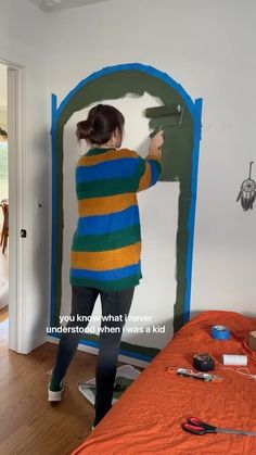 a woman is painting a wall in her bedroom with blue and green stripes on it