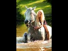 a woman riding on the back of a white horse through a body of water with splashing water around her