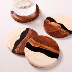 three wooden coasters sitting on top of a white table next to a glass filled with liquid