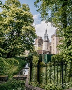 an old castle surrounded by lush green trees and bushes with a river running through it