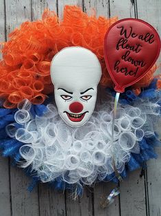 an orange and white clown mask hanging on a door wreath with words written on it