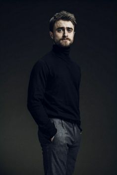 a man standing with his hands in his pockets and wearing a black turtle neck sweater