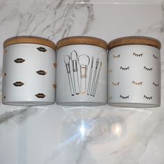 three canisters with eyelashes and scissors on them sitting on a marble counter top