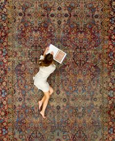 a woman laying on top of a rug with an open book in her hand and reading