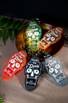 four keychains with different designs on them sitting next to a leafy plant