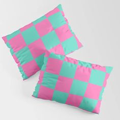 two pink and blue checkered pillows sitting on top of eachother in front of a white wall