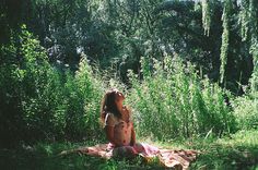 a woman sitting on top of a blanket in the middle of a forest next to tall grass