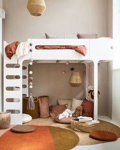 a white bunk bed sitting in a bedroom next to a rug on the floor and pillows