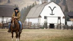 a woman riding on the back of a brown horse in front of a white barn