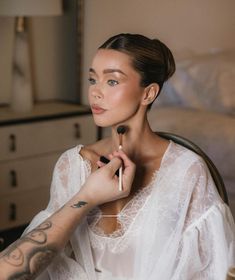 a woman sitting in a chair holding a brush and looking at the camera while she is getting her makeup done