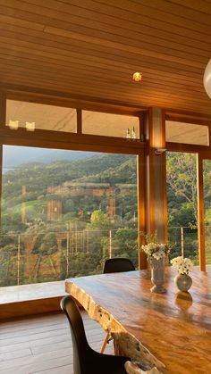 a wooden table with chairs and vases on top of it in front of large windows