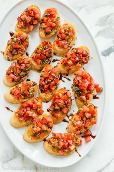 small appetizers with tomatoes and herbs are on a white platter, ready to be eaten