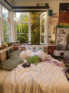 an unmade bed in front of two windows with posters on the wall behind it