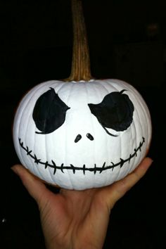 a hand holding a jack - o'- lantern pumpkin with black eyes and nose