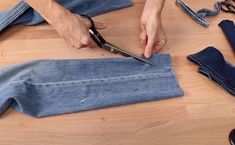 someone cutting up some jeans with scissors on a wooden floor next to other clothing items