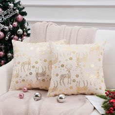 two christmas pillows sitting on top of a couch next to a christmas tree and ornaments