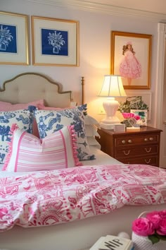 a bed with pink and blue pillows in a bedroom next to a lamp on a dresser