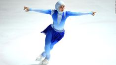 a woman skating on an ice rink wearing a blue outfit and white headdress