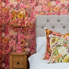 a bed with pink and yellow floral wallpaper next to a lamp on a night stand