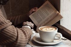 a person sitting at a table with a cup of coffee and an open book