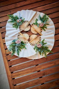 paper plates with flowers and greenery are arranged on a wooden table top in the shape of a fan