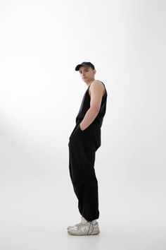 a man standing in front of a white background wearing a hat and black jumpsuit