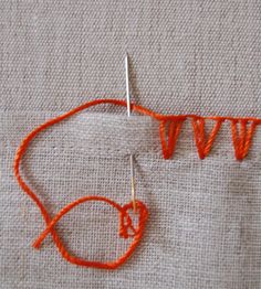 an orange piece of fabric with some thread on it and two knitting needles in the middle