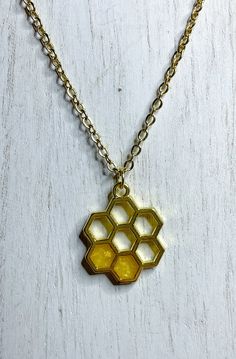 "Bee happy! This honeycomb pendant necklace is sure to make you smile. Gold honeycomb charm partially filled with gold resin that resembles honey. On an 18\" gold finished chain necklace.  Makes wonderful and thoughtful Christmas, birthday, or Mother's Day gifts. Or as a special treat for yourself!  This listing is for the necklace only. Please check our listings for matching earrings to complete the set.  Beehive honeycomb earrings: https://kwmandco.etsy.com/listing/1346434656/ Small honeycomb earrings: https://kwmandco.etsy.com/listing/1244253499/ To preserve the life of your resin jewelry and keep it from tarnishing and discoloring, please remove before showering, swimming, or heavy exercise. Take care not to wear while applying lotions, creams, or perfumes. When not wearing, store your Gold Hexagon Necklace, Honey Necklace, Honeycomb Earrings, Bee Necklace Cute, Honeycomb Necklace, Bee Pendant, Honeycomb Pattern, Hippie Necklace, Bee Happy