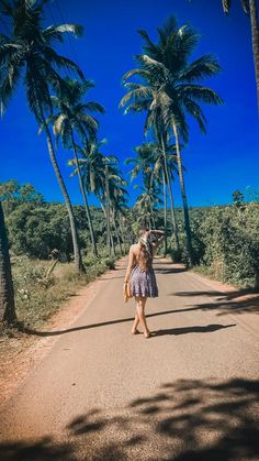 a woman walking down the middle of a road with palm trees in the back ground