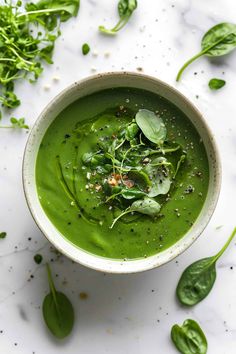 a white bowl filled with green soup and garnished with herbs