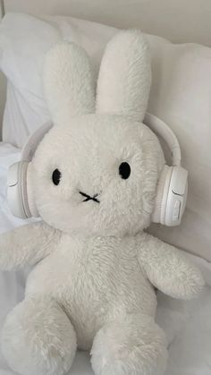 a white stuffed rabbit with headphones on it's ears sitting on a bed