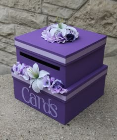 two purple boxes with flowers on them sitting next to a stone wall, one has the word cards written on it