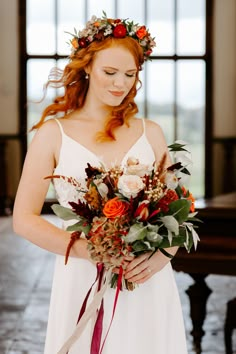 a woman in a white dress holding a bouquet of red and orange flowers on her wedding day