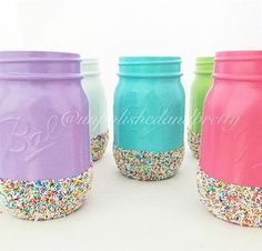 four mason jars filled with sprinkles and colored lids are lined up in a row