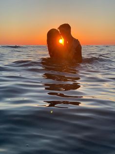 two people are kissing in the ocean at sunset or sunrise, with their backs to each other