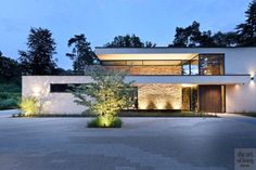 a modern house lit up at night with lights on the windows and plants in front