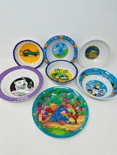 various children's plates and bowls with pictures of cartoon characters are arranged on a white surface