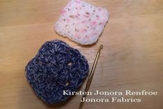 two crocheted items sitting on top of a wooden table next to knitting needles