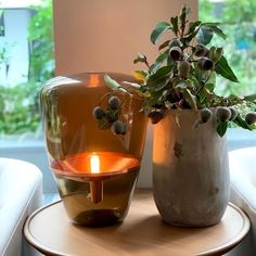 two vases sitting on top of a wooden table next to a candle and potted plant