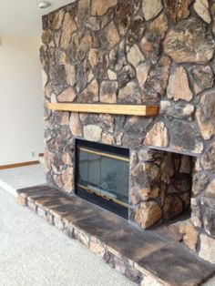 a stone fireplace in the middle of a living room with carpeted floor and white walls