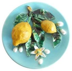 two lemons and leaves on a blue plate with white flower petals in the center