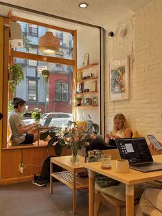 two people sitting at a table with laptops in front of them, looking out the window